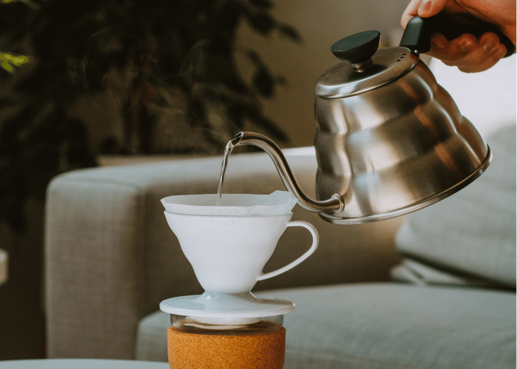 best gooseneck kettle, photo of someone using a silver gooseneck kettle to make pour over coffee in a white mug