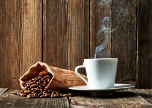 How long do roasted coffee beans last, photo of a bag of coffee beans spilling over and a hot cup of coffee in a white mug next to it with a wooden background.