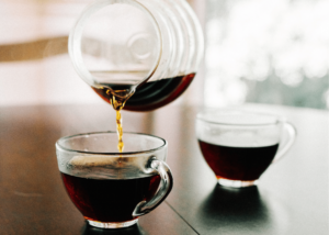 how to make low acid coffee, photo of two clear glass coffee mugs sitting on a table and a clear coffee pot pouring coffee into one.