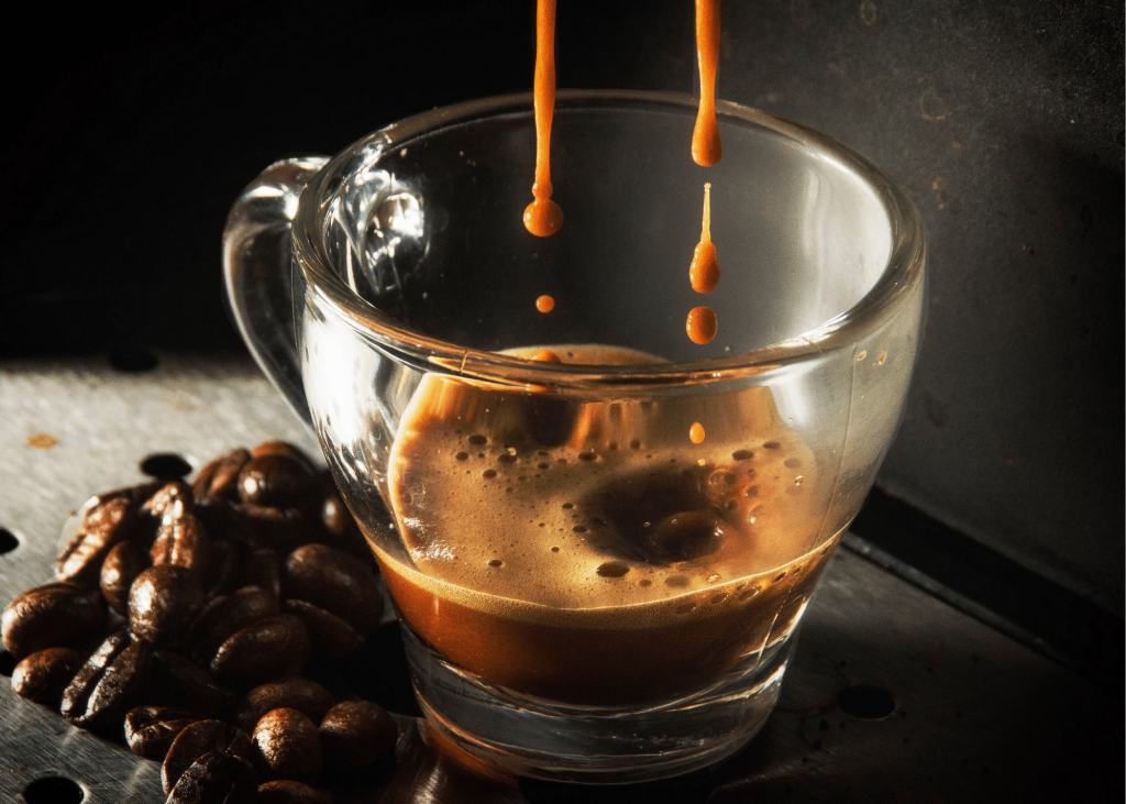 espresso dripping into a clear mug, coffee beans sitting next to the mug and a dark background. Article keyword: delonghi magnifica
