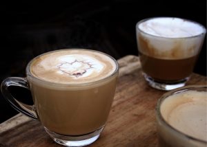 latte vs cappuccino, two clear mugs on sitting on a wooden table top one cappuccino and one latte next to eachother